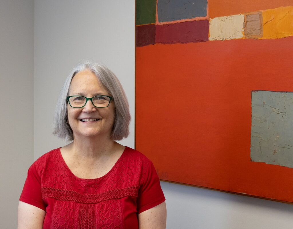 Paula Arscott smiles next to a painting.