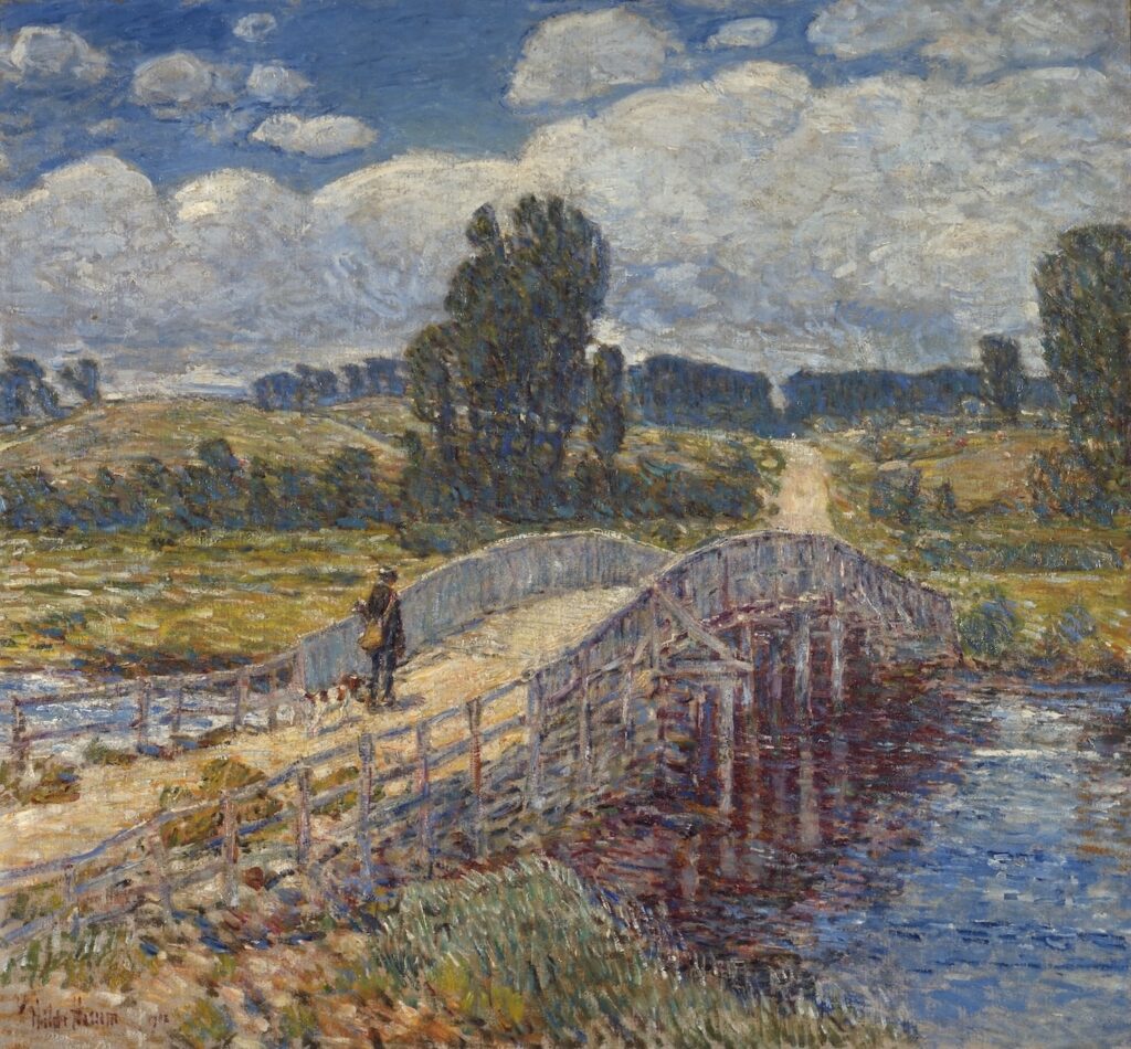 Childe Hassam's impressionist oil painting "Bridge at Old Lyme" shows a person wearing a messenger bag walking with a brown and white dog. They are about to cross the Bow Bridge in Old Lyme, Connecticut. The sky is deep blue with fluffy white clouds.
