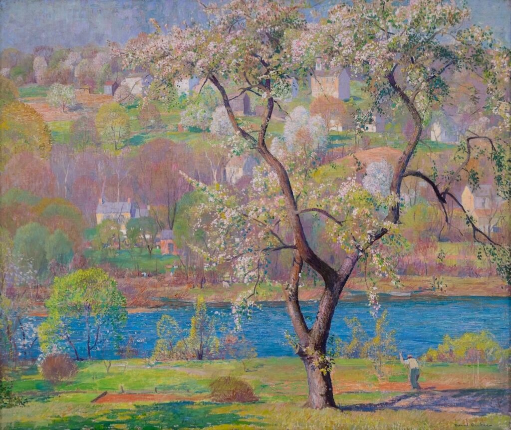 Daniel Garber's oil painting "Spring Panel" shows a man standing next to a blooming tree on the bank of a river. Across the river, houses are scattered across the hillside.